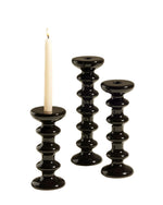 Trois bougeoirs Slave Noir en faïence minérale, design totémique, avec une bougie allumée.