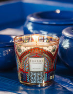 Bougie parfumée Baobab Collection Marrakech, verre coloré aux motifs architecturaux marocains, flamme allumée.