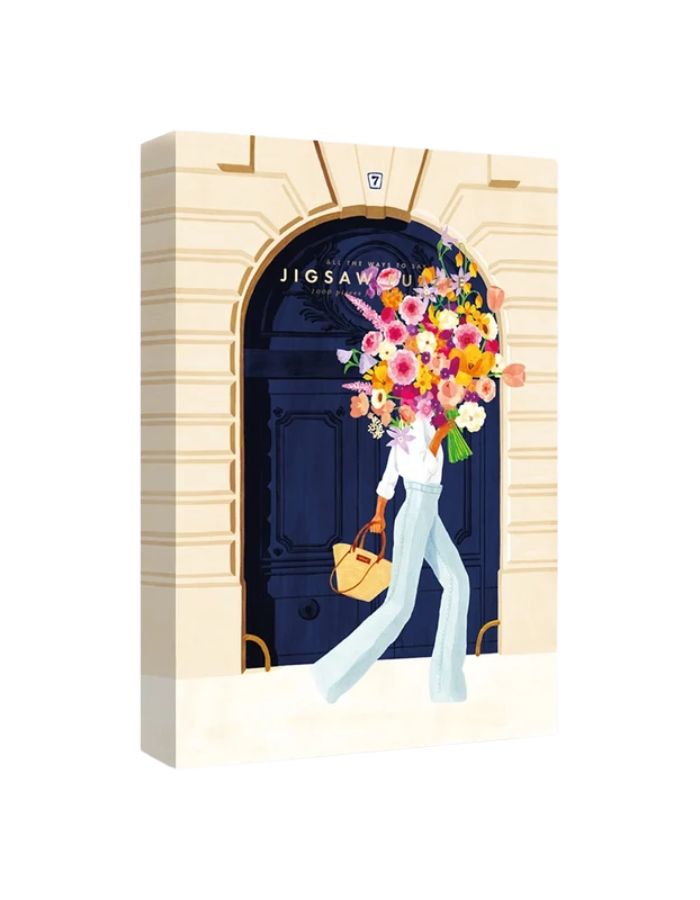 Boîte et puzzle assemblé de 1000 pièces Parisian Door par All The Ways To Say montrant une femme avec un bouquet de fleurs devant une porte cochère bleue à Paris