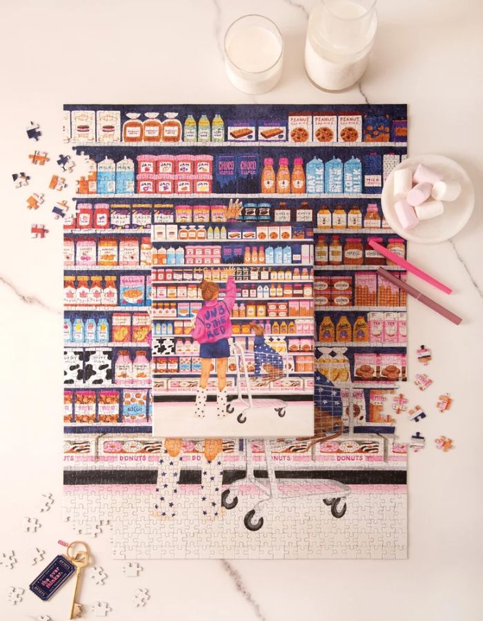 Ambiance avec la Boîte et puzzle assemblé de 1000 pièces Sugar Market par All The Ways To Say montrant une jeune fille dans une épicerie colorée avec son chien dans le caddie.