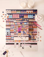 Ambiance avec la Boîte et puzzle assemblé de 1000 pièces Sugar Market par All The Ways To Say montrant une jeune fille dans une épicerie colorée avec son chien dans le caddie.