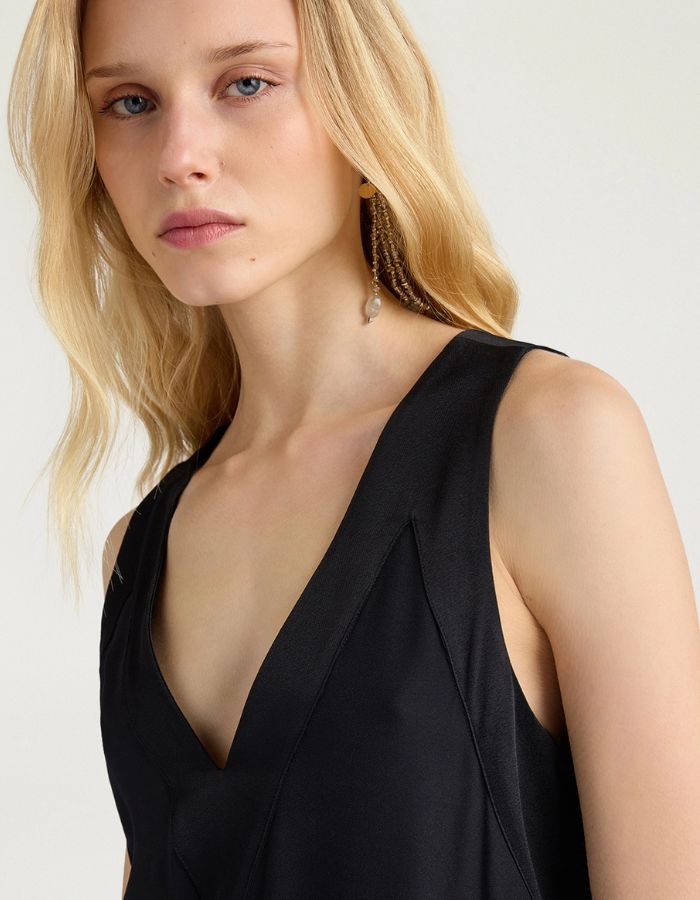 Haut de la Robe mi-longue sans manches en satin de viscose noir, modèle Eisla de la marque MOMONI. Présente une coupe fluide évasée, un décolleté V satiné brillant et un nœud à la nuque
