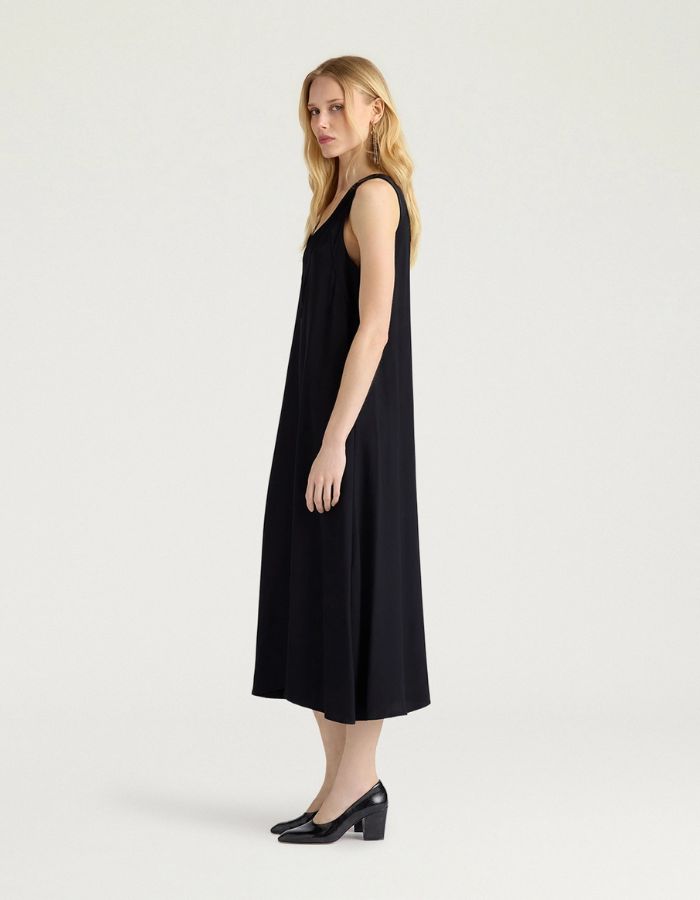 Profil de la Robe mi-longue sans manches en satin de viscose noir, modèle Eisla de la marque MOMONI. Présente une coupe fluide évasée, un décolleté V satiné brillant et un nœud à la nuque