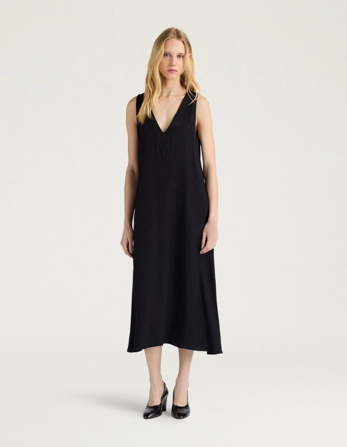 Silhouette avec la Robe mi-longue sans manches en satin de viscose noir, modèle Eisla de la marque MOMONI. Présente une coupe fluide évasée, un décolleté V satiné brillant et un nœud à la nuque