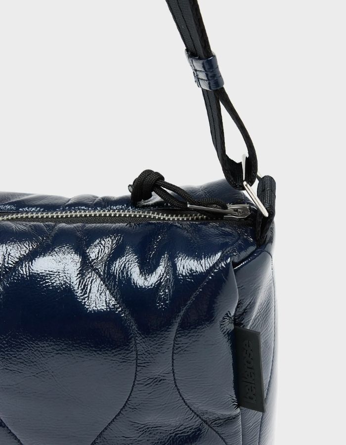 Zip du Sac bandoulière matelassé pour femme en tissu aspect vinyle brillant bleu marine navy avec fermeture zippée et patch en silicone, modèle Hobbes Crossbody Bag de la marque Bellerose.