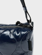 Zip du Sac bandoulière matelassé pour femme en tissu aspect vinyle brillant bleu marine navy avec fermeture zippée et patch en silicone, modèle Hobbes Crossbody Bag de la marque Bellerose.