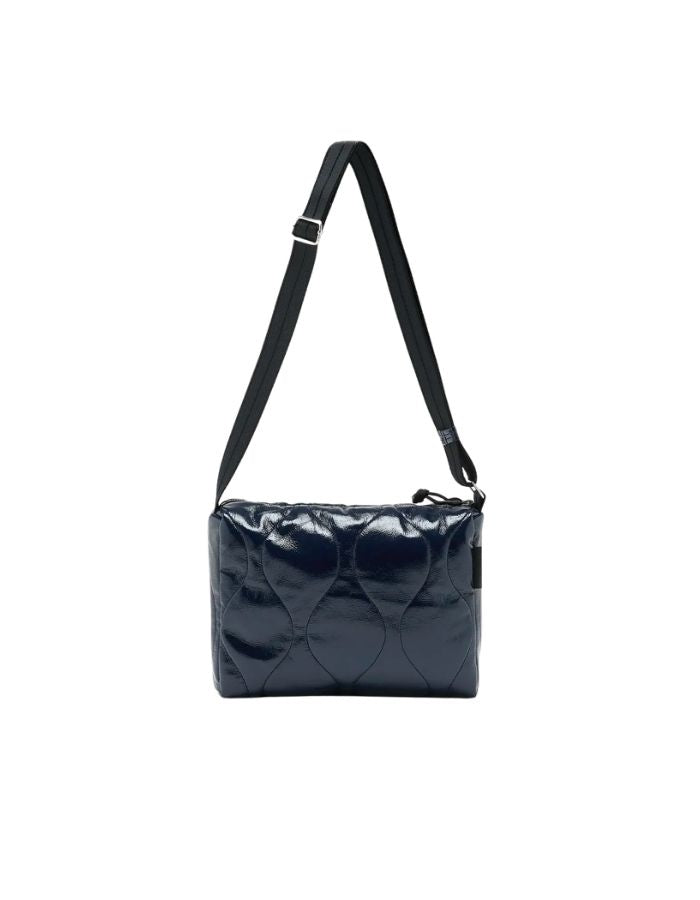 Sac bandoulière matelassé pour femme en tissu aspect vinyle brillant bleu marine navy avec fermeture zippée et patch en silicone, modèle Hobbes Crossbody Bag de la marque Bellerose.
