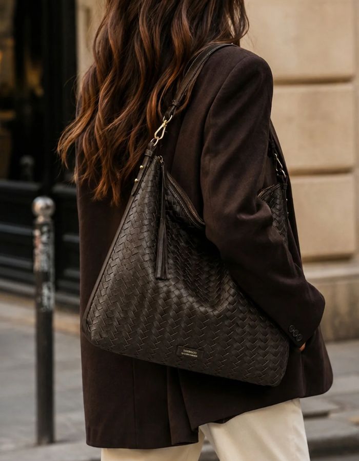 Silhouette avec le Sac hobo pour femme en cuir de vachette tressé marron chocolat avec pompon assorti, modèle Sharon de LOXWOOD. Porté épaule avec fermeture zippée.