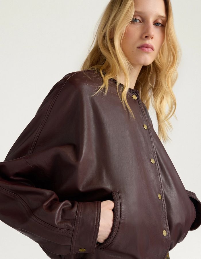 Manche de la Veste bomber courte pour femme en cuir d'agneau marron, modèle Kaldor de la marque MOMONI. Présente une coupe carrée avec cordon de serrage au bas et des boutons-pression en laiton vieilli.