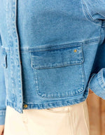 Poche de la Veste courte en jean bleu stone pour femme avec col montant et broderie en relief dans le dos, modèle Velmo de La Petite Étoile. Présente des poches à rabat et une coupe droite.