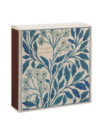Côté de la Grande boîte d'allumettes carrée de la marque Archivist au design floral bleu et blanc vintage avec l'inscription gravée en lettres dorées 'Luxury Matches'. À côté, le tiroir blanc est entrouvert, laissant apparaître de longues allumettes en bois naturel à tête blanche.