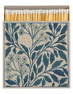 Grande boîte d'allumettes carrée ouverte de la marque Archivist au design floral bleu et blanc vintage avec l'inscription gravée en lettres dorées 'Luxury Matches'. À côté, le tiroir blanc est entrouvert, laissant apparaître de longues allumettes en bois naturel à tête blanche.