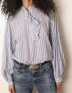 Col de la Blouse ample pour femme en coton bleu à rayures, modèle Fa de la marque Laurence Bras. Présente un col rond, des volants asymétriques sur le devant et des manches bouffantes.