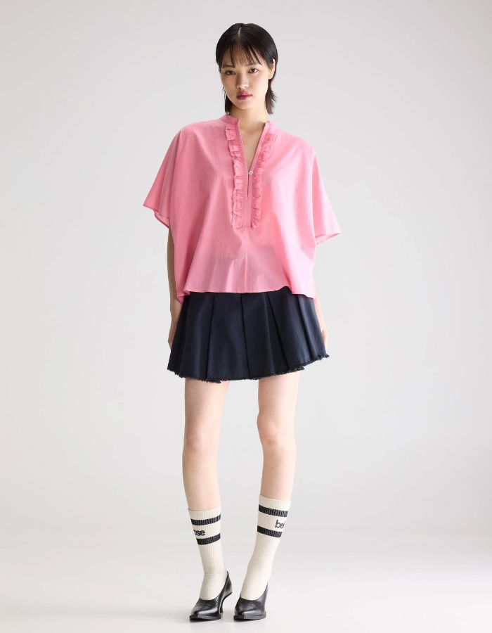 Blouse Dahlia Geranium rose oversized en voile de coton avec col mandarin et volants, portée avec une jupe noire.
