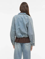 Dos du Blouson style bomber en jean pour femme de couleur bleu clair délavé Light Blue Denim, modèle Tiana de la marque Rouge Edit. Présente un col chemise évasé, une fermeture à glissière cachée sous des boutons-pression dorés mats Dull Gold et des brides de serrage ajustables.