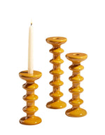 Trois bougeoirs Slave Fauve en faïence minérale ambrée, un avec bougie allumée, design totémique.