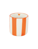 Gros plan sur la Bougie parfumée d'intérieur Chichou de la marque Opjet, logée dans un contenant cylindrique en céramique blanche de 8 cm de diamètre avec des rayures horizontales orange peintes à la main