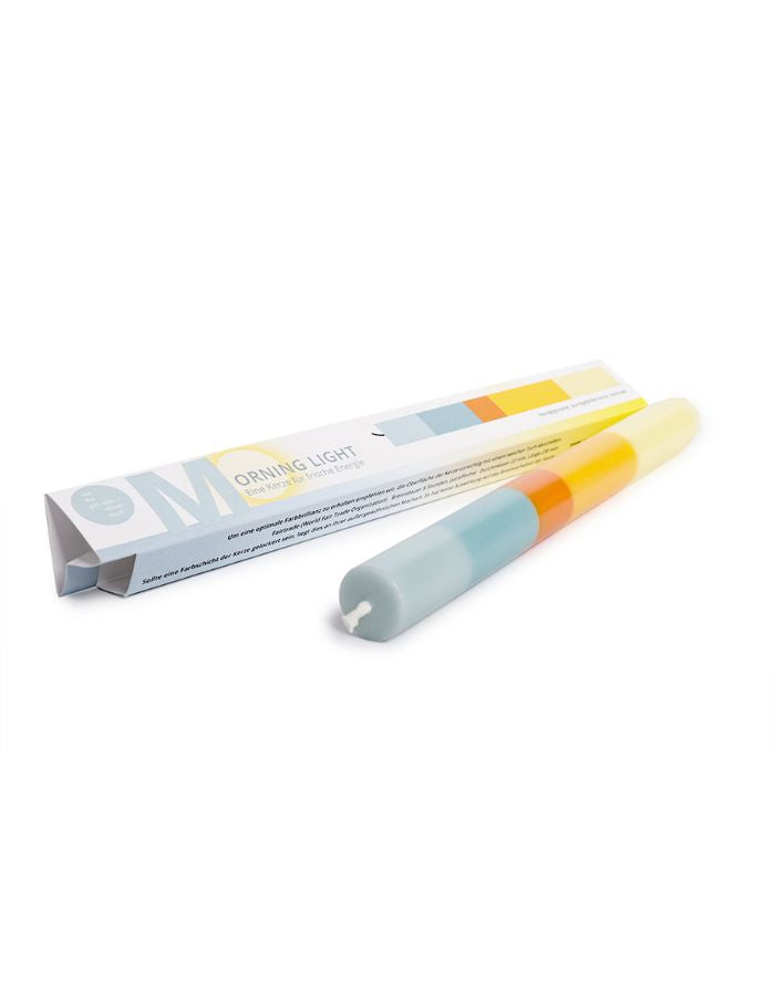 Emballage de la Bougie de type flambeau fine et élancée modèle Morning Light de 23 cm de haut. Présente un design minimaliste avec des couches de cire végétale colorées superposées à la main, posée à côté de son étui en papier de création certifié FSC