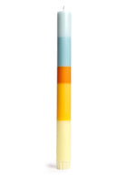 Bougie de type flambeau fine et élancée modèle Morning Light de 23 cm de haut. Présente un design minimaliste avec des couches de cire végétale colorées superposées à la main, posée à côté de son étui en papier de création certifié FSC