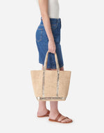 Cabas M en raphia or avec sequins dorés, porté main par une femme en jean et sandales.
