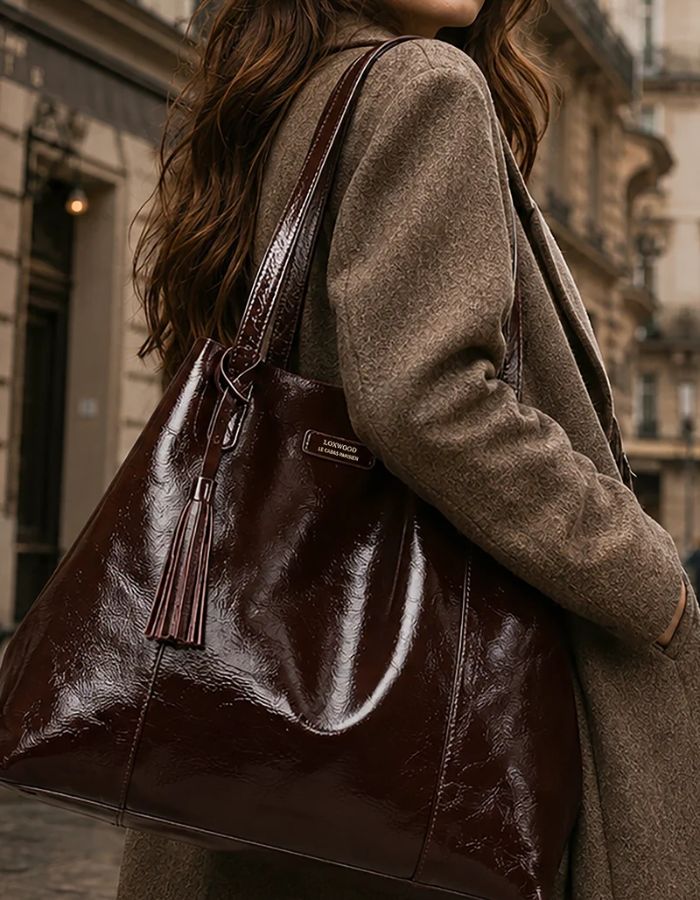 Silhouette avec le Grand sac cabas souple pour femme en cuir de vachette vernis bordeaux, modèle Odéon de la marque LOXWOOD. Présente deux anses de porté épaule, une patte de fermeture magnétique et un pompon amovible en cuir.
