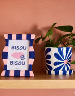 Ambiance déco avec le Cache-pot rond en céramique dolomite fait main Lior de la marque Qué Rico, posé sur sa coupelle de drainage assortie. Décoré d'un motif de fleurs graphiques peintes à la main dans des nuances de bleu vif et bleu marine.