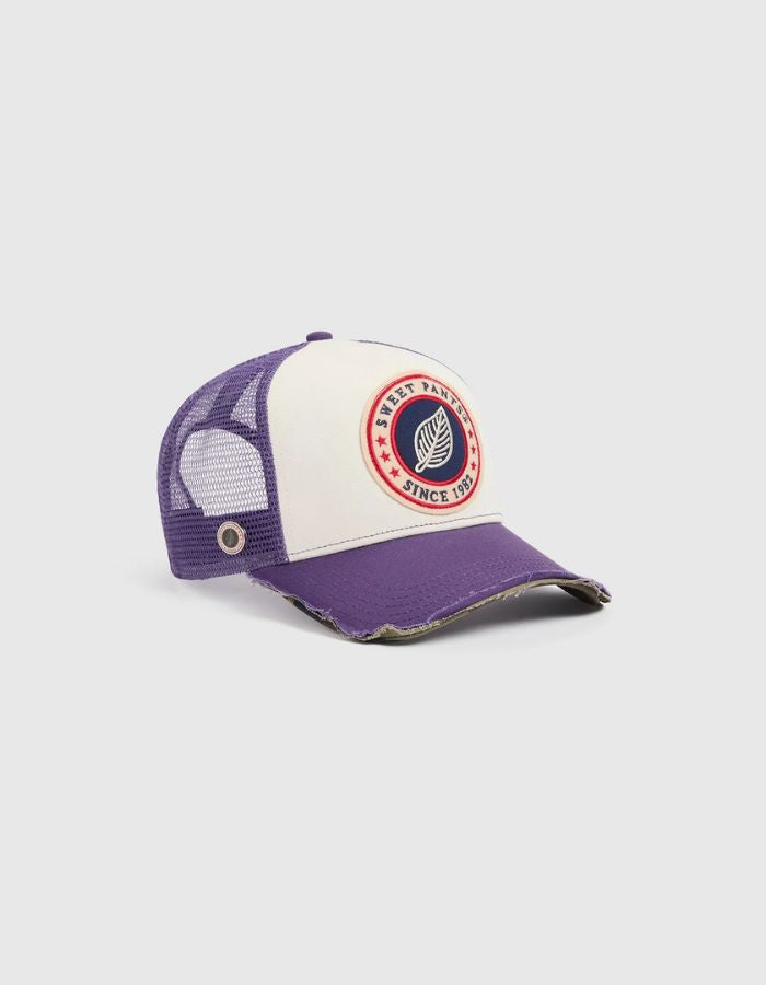Vue de côté de la Casquette Trucker bicolore Home Run par Sweet Pants, coloris violet Imperial et blanc. Patch logo de la marque cousu à l'avant, visière violette avec bordure effet usé et panneau arrière en maille filet blanc.