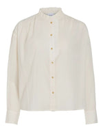 Chemise unie pour femme modèle Esma Frill de la marque Vila. Coupe droite à manches longues en coton bio de couleur blanc cassé écru Birch, ornée de volants plissés délicats le long du col et de la boutonnière.