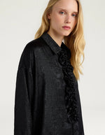Col du Chemisier long fluide noir pour femme au fini métallisé laminé brillant, modèle Bilancia Bis de la marque Momoni. Présente une coupe oversize avec de grands volants drapés, un col bateau asymétrique tombant sur l'épaule et des manches longues terminées par de hauts poignets à boutons recouverts.