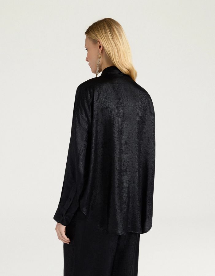 Dos du Chemisier long fluide noir pour femme au fini métallisé laminé brillant, modèle Bilancia Bis de la marque Momoni. Présente une coupe oversize avec de grands volants drapés, un col bateau asymétrique tombant sur l'épaule et des manches longues terminées par de hauts poignets à boutons recouverts.