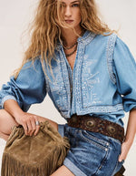 Chemise Laura Ba&sh en denim clair avec broderies blanches, manches bouffantes, portée avec un short en jean et une ceinture marron.