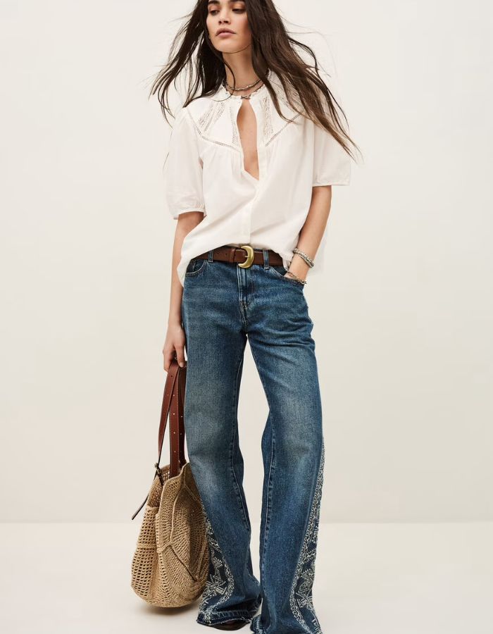 Chemise Nella Ecru en voile de coton biologique avec dentelle, manches courtes, portée avec un jean et un sac en paille.