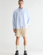 Homme portant une chemise LIGHTO rayée bleu clair et blanc en coton, ouverte sur un t-shirt blanc.
