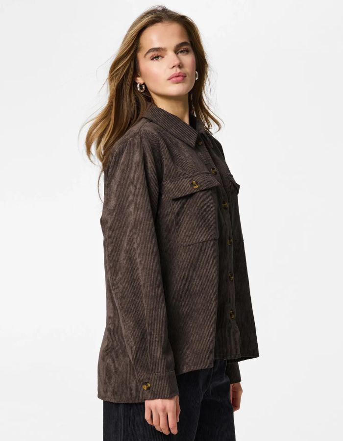 Vue de profil de la Chemise ample pour femme en velours côtelé à manches longues, modèle Effi de la marque Pieces. Tissu corduroy de couleur marron foncé chocolat Hot Fudge, avec des poches de poitrine boutonnées et des poignets élastiqués.