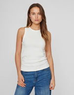 Femme portant un débardeur blanc côtelé en coton biologique Sola, coupe ajustée, avec un jean bleu.