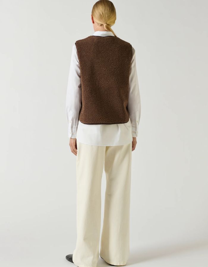 Vue de dos du Gilet sans manches pour femme en fausse fourrure de couleur marron foncé, modèle Fusil de la marque Soeur. Présente une coupe droite dotée d'une encolure en V, d'une fermeture boutonnée à l'avant, de deux poches passepoilées et de bordures proprement gansées.