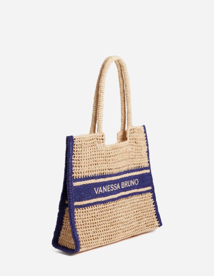 Grand panier en raphia beige tressé avec motif ajouré, bandes bleu marine contrastées et logo Vanessa Bruno brodé.