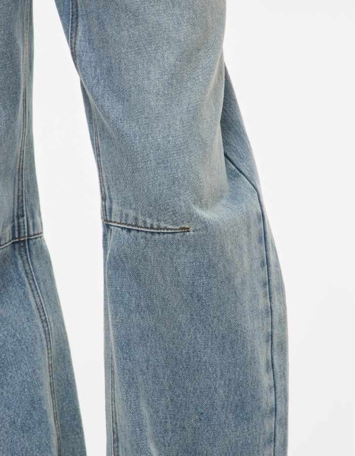 Détail de la jambe du Jean pour femme de couleur bleu clair délavé Light Blue Denim, modèle Tiana de la marque Rouge Edit. Présente une coupe droite ample contemporaine, une taille mi-haute avec des passants de ceinture et des finitions de boutons en métal doré mat Dull Gold.