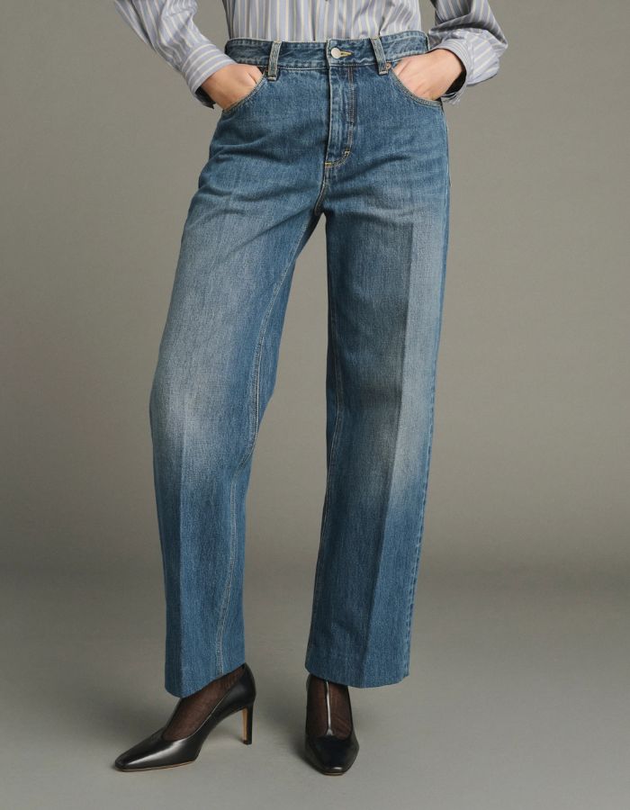 Vue de face du Jean droit pour femme en denim bleu délavé avec plis marqués devant et dos, modèle Jerry de la marque SOEUR. Présente une coupe droite 5 poches, une fermeture boutonnée zippée et un patch en cuir au dos.