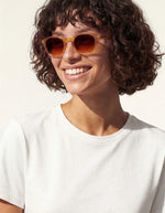 Femme avec les Lunettes de soleil unisexes IZIPIZI modèle #C de forme carrée vintage épaisse. La monture brillante arbore une couleur miel ocre ambrée et translucide nommée Golden Canyon, associée à des verres solaires polarisés protecteurs.