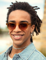 Homme avec les Lunettes de soleil unisexes IZIPIZI modèle #C de forme carrée vintage épaisse. La monture brillante arbore une couleur miel ocre ambrée et translucide nommée Golden Canyon, associée à des verres solaires polarisés protecteurs.