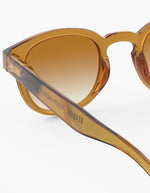 Verre des Lunettes de soleil unisexes IZIPIZI modèle #C de forme carrée vintage épaisse. La monture brillante arbore une couleur miel ocre ambrée et translucide nommée Golden Canyon, associée à des verres solaires polarisés protecteurs.