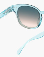 Gros plan sur les Lunettes de soleil unisexes IZIPIZI modèle #C de forme carrée vintage épaisse. La monture brillante est d'une couleur bleu turquoise translucide inspirée de la pierre turquoise, associée à des verres solaires bleus.
