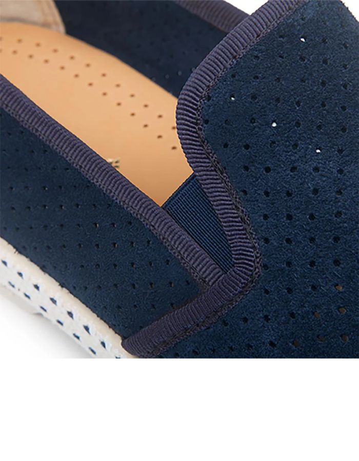Détail des Mocassins Rivieras Classic en daim bleu marine perforé. Semelle blanche contrastée avec couture selle en coton, élastiques de confort et rivet métallique logoté sur le côté. Design intemporel fabriqué en Espagne.