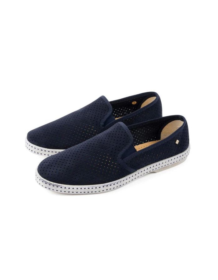 Paire de Mocassins Rivieras Classic en daim bleu marine perforé. Semelle blanche contrastée avec couture selle en coton, élastiques de confort et rivet métallique logoté sur le côté. Design intemporel fabriqué en Espagne.