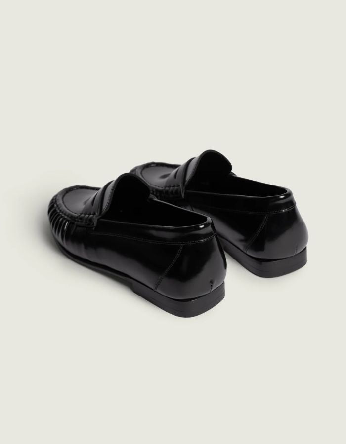 Talon des Mocassins en cuir noir brillant pour homme et femme de type Penny Loafers, modèle Wrinkle de la marque POSA. Chaussures basses en cuir italien box poli avec une bride classique sur le coup de pied, un bout arrondi à empiècement plissé texturé et une semelle noire fine.