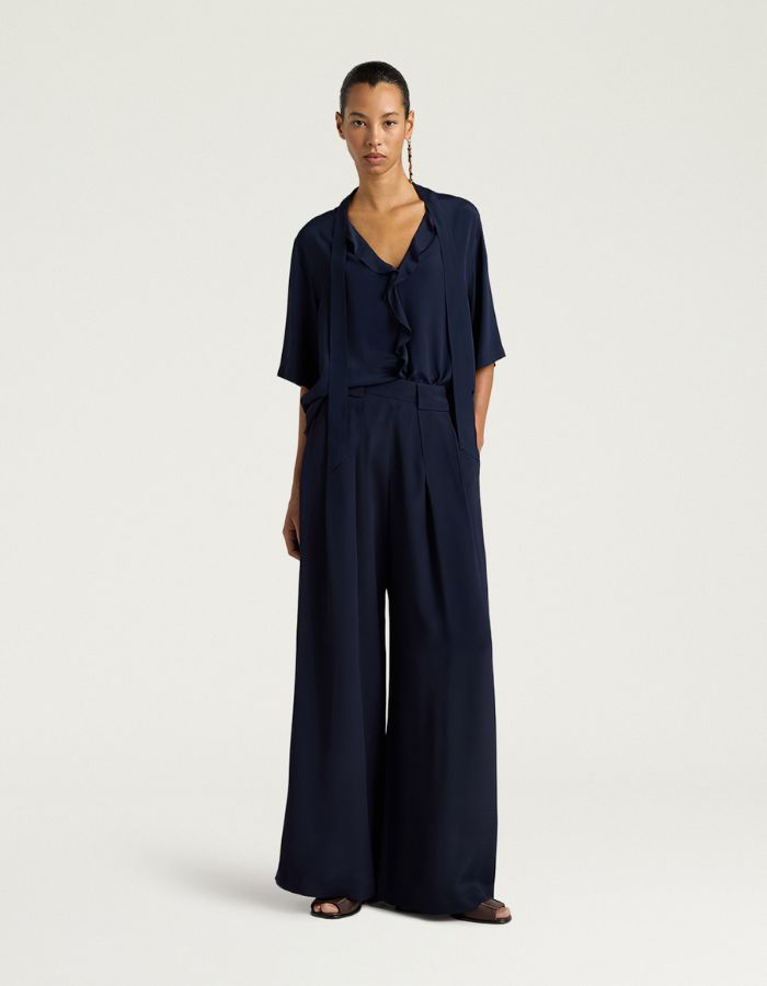 Silhouette avec le Pantalon large fluide style palace Aspen de la marque Momoni, coloris bleu uni. Coupe ample en crêpe d'acétate de soie avec plis élégants sur le devant, maxi passants à la taille et poches latérales.