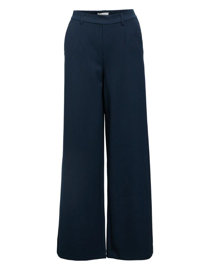 Pantalon large pour femme de couleur bleu marine foncé Sky Captain, modèle Lisa Wide Pant de la marque Object. Présente une coupe droite très ample de style wide-leg, une taille mi-haute froncée par un élastique confortable et des poches discrètes insérées dans les coutures latérales.