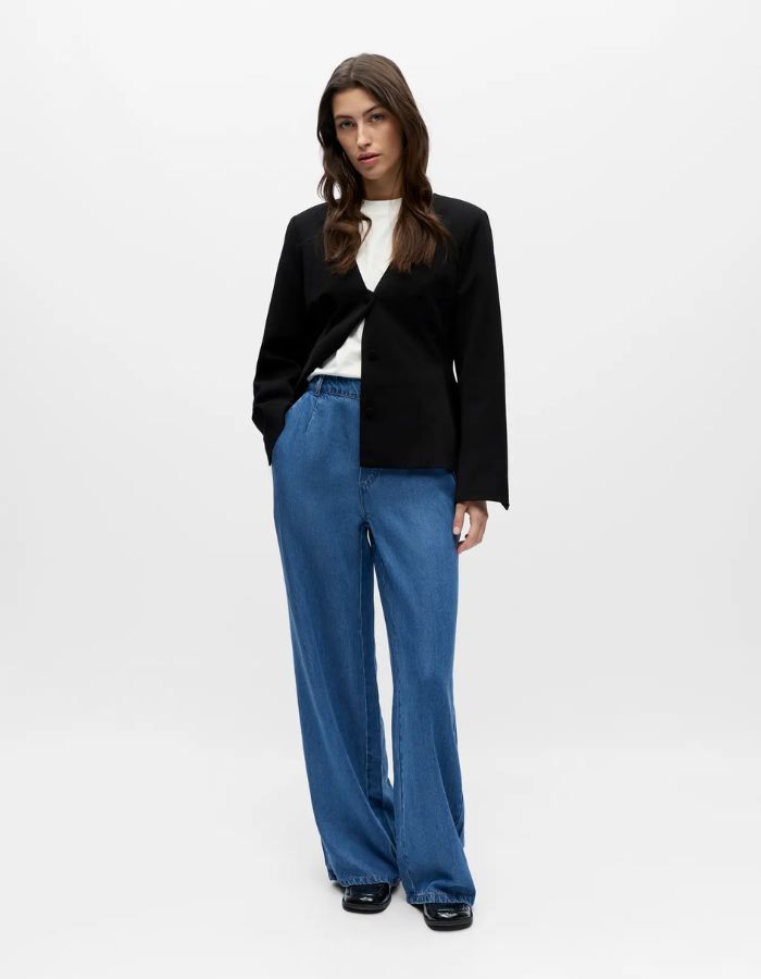 Femme portant un pantalon large fluide denim Frame bleu, taille mi-haute, avec un blazer noir et un t-shirt blanc.