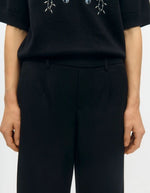 Ceinture du Pantalon large pour femme de couleur noir uni opaque, modèle Lisa Wide Pant de la marque Object. Présente une coupe droite très ample de style wide-leg, une taille mi-haute froncée par un élastique confortable et des poches discrètes insérées dans les coutures latérales.